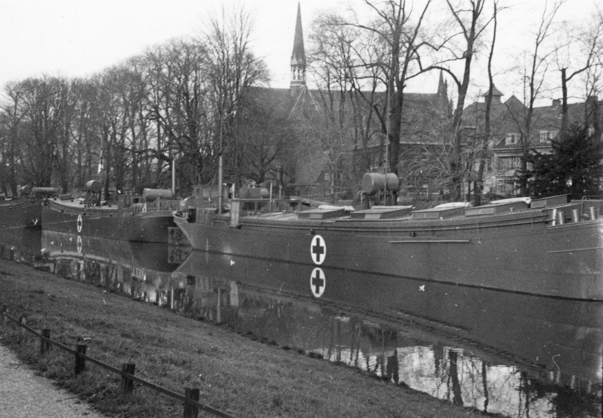 Afbeelding van enkele binnenvaartschepen met het logo van het Rode Kruis, in de Stadsbuitengracht ter hoogte van het Stads- en Academisch Ziekenhuis (Catharijnesingel 101) te Utrecht: op de achtergrond de St.-Martinuskerk (Oudegracht 401).